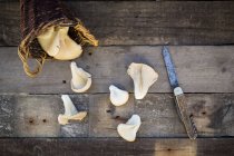 Wickerbasket of oyster mushrooms and a pocket knife on wood — Stock Photo