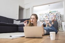 Jeune femme à la maison couchée sur le sol à l'aide d'un ordinateur portable — Photo de stock