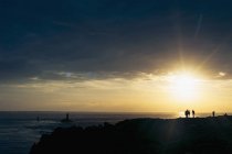 Francia, Bretagna, Pointe du Raz, persone che guardano il tramonto sulla costa con i fari Phare de la Vieille e Phare de Tevennec — Foto stock