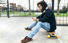 Giovane skateboarder barbuto con smartphone e cuffie — Foto stock