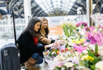 Two young women admiring flowers at train station, London, UK — Stock Photo
