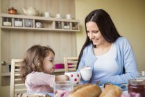 Madre e hija pequeña brindando con tazas - foto de stock