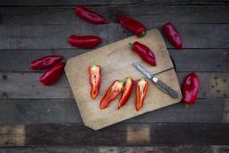 Chopped and whole red pointed peppers on wooden chopping board — Stock Photo