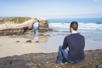 Іспанія, Ribadeo, спині подання людина сидить на скелях Playa de Las Catedrales — стокове фото