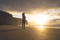 Frau steht bei Sonnenuntergang am Strand — Stockfoto