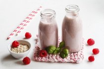 Bouteilles en verre de milk-shakes framboises avec flocons d'avoine et basilic — Photo de stock