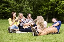 Happy friends with guitar and beer bottles relaxing in park — Stock Photo