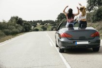 Mulheres se divertindo em um carro conversível em uma estrada rural — Fotografia de Stock