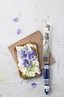 Slice of wholemeal bread with cream cheese, chives and edible Horned Violets — Stock Photo