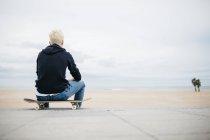 Young man sitting on skateboard — Stock Photo