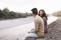 Молода пара сидить перед річкою — стокове фото
