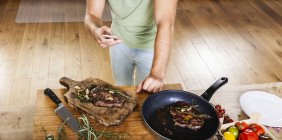 Man with prepared steaks in kitchen using celll phone — Stock Photo