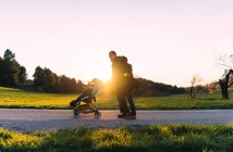 Couple walking with baby in stroller at sunset — Stock Photo