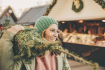 Mulher feliz com árvore embrulhada andando no Mercado de Natal — Fotografia de Stock