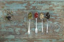 Row of four silver spoons with different sorts of peppercorns — Stock Photo