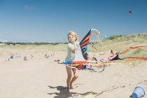 Blond boy holding flying kite on beach — Stock Photo