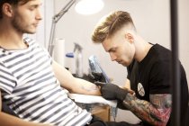 Татуировщик на работе в своей тату-студии с клиентом — стоковое фото