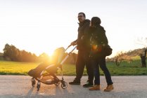 Couple on a walk with their baby in the stroller at sunset — Stock Photo