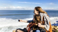 Две молодые женщины развлекаются со смартфоном у моря — стоковое фото