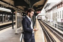 Молодий підприємець очікування на станції метро платформа, за допомогою смартфона — стокове фото