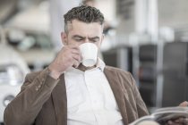 Человек пьет кофе читает журнал в автосалоне — стоковое фото