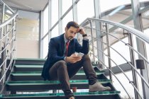 Pensive businessmann sentado nas escadas olhando para o telefone celular — Fotografia de Stock