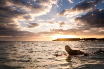 Teenager surft bei Sonnenuntergang im Meer — Stockfoto