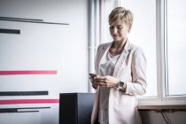 Businesswoman at the window looking at cell phone — Stock Photo