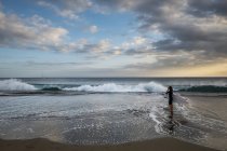 Vue lointaine de adolescent garçon debout avec planche de surf sur la plage — Photo de stock