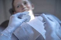 Dentiste tenant fil dentaire avec garçon en chirurgie dentaire en arrière-plan — Photo de stock