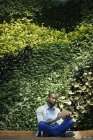 Joven hombre de negocios utilizando tableta digital frente a la pared de la planta verde - foto de stock