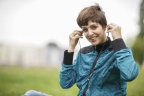 Portrait of smiling young woman with earphones sitting on a meadow — Stock Photo