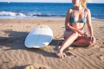 Giovane surfista seduta sulla spiaggia sabbiosa e guardando lateralmente — Foto stock