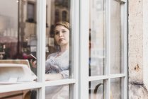 Junge Frau mit Tablet und Handy in einem Café, das aus dem Fenster schaut — Stockfoto