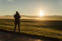 Mulher fotografando o nascer do sol em pé no campo de verão — Fotografia de Stock