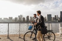 Dois homens de negócios com bicicleta andando ao longo de East River, Nova York, EUA — Fotografia de Stock