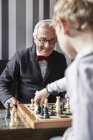 Abuelo y nieto jugando ajedrez en casa - foto de stock