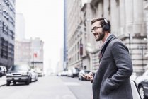 Lächelnder Geschäftsmann mit Handy und Kopfhörer unterwegs, New York City, USA — Stockfoto
