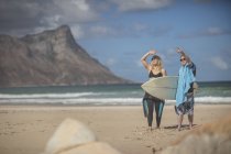 Adolescent avec syndrome du duvet et femme avec planche de surf sur la plage — Photo de stock