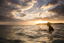 Adolescente nadando na prancha de surf no oceano ao pôr do sol bonito — Fotografia de Stock