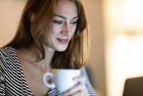 Retrato de mulher sorridente com xícara de café usando laptop — Fotografia de Stock