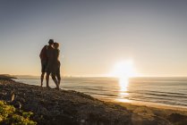 Rückansicht eines verliebten jungen Paares beim Sonnenuntergang am Meer — Stockfoto