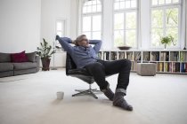 Homme mûr détendu assis sur une chaise à la maison — Photo de stock