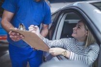 Lächelnde Kundin im Auto füllt in der Werkstatt Formular auf Klemmbrett aus — Stockfoto