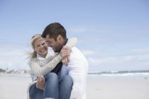 Улыбающийся мужчина держит женщину на пляже — стоковое фото