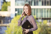 Portrait d'une femme d'affaires rousse tenant un fichier téléphonique avec un smartphone — Photo de stock