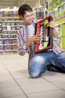Portrait of happy man crouching on the floor of a supermarket playing with toy keyboard — Stock Photo