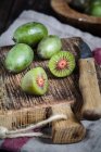 Sliced and whole mini kiwis and a kitchen knife on wooden chopping board — Stock Photo