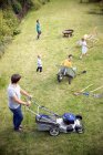 Vater mäht Rasen im Garten, Familie spielt im Gras — Stockfoto