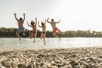 Amici felici che saltano nel fiume sulla spiaggia — Foto stock